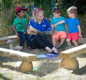 Reading a book with three children in the garden